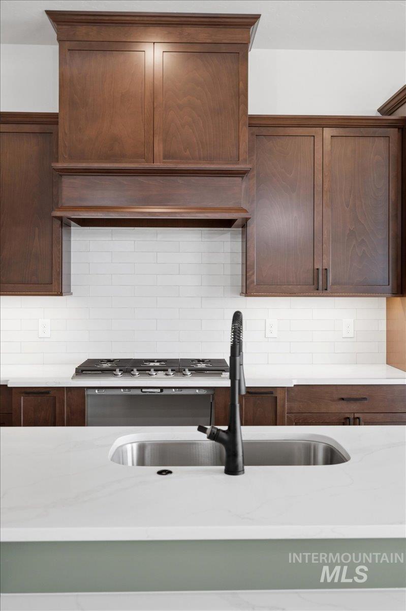 6431 Raptor Ridge Lane Melba, ID 83641 - Photo 16 of 50 Kitchen with light stone counters, decorative backsplash, range hood, and dark wood finish cabinets