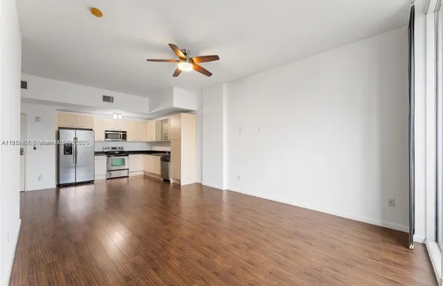 a view of an empty room with wooden floor a ceiling fan and windows