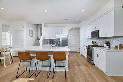a kitchen with stainless steel appliances granite countertop a stove top oven a sink dishwasher a refrigerator and white cabinets with wooden floor