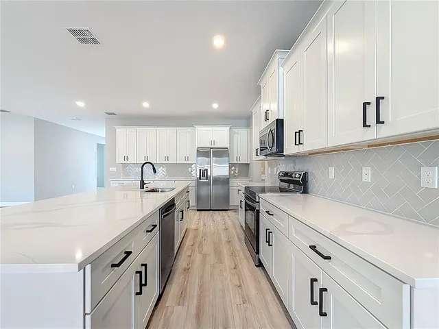 a large kitchen with stainless steel appliances granite countertop a stove a sink dishwasher and a oven with white cabinets
