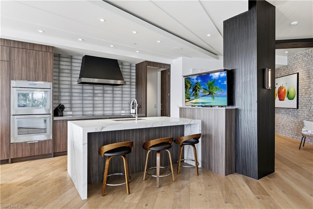 909 10th Street South, Unit 201 Naples, FL 34102 - Photo 6 of 42 Dual tone kitchen with light stone counters, a breakfast bar area, a kitchen island with sink, stainless steel double oven, and modern cabinets