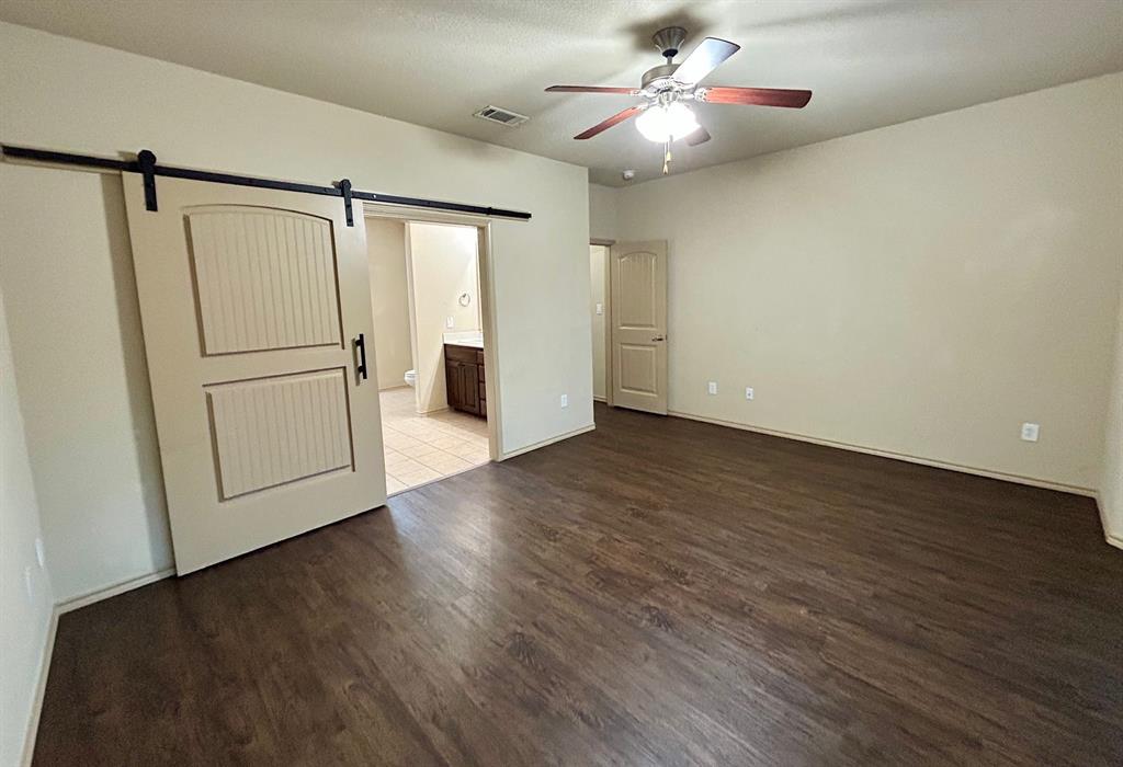 3105 Pecan Tree Drive Denton, TX 76210 - Photo 13 of 25 Unfurnished bedroom with a barn door, dark wood-style floors, ensuite bath, and ceiling fan