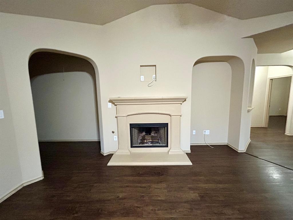 3105 Pecan Tree Drive Denton, TX 76210 - Photo 6 of 25 Unfurnished living room with arched walkways, dark wood-type flooring, a fireplace with raised hearth, and vaulted ceiling