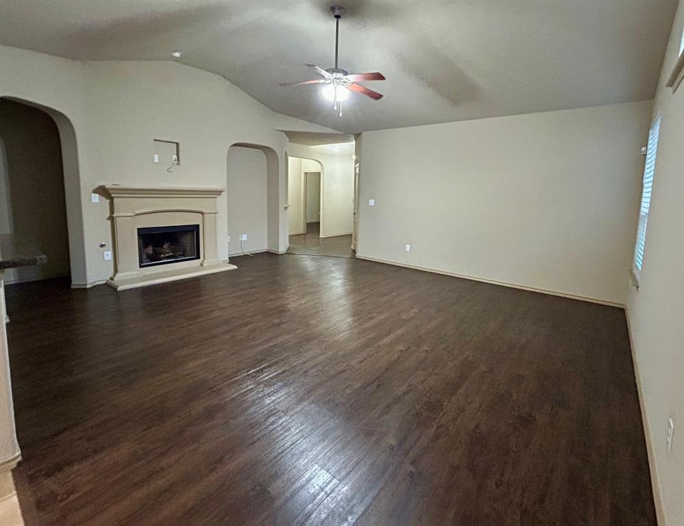 3105 Pecan Tree Drive Denton, TX 76210 - Photo 8 of 25 Unfurnished living room with dark wood-style flooring, a fireplace with raised hearth, vaulted ceiling, a ceiling fan, and arched walkways
