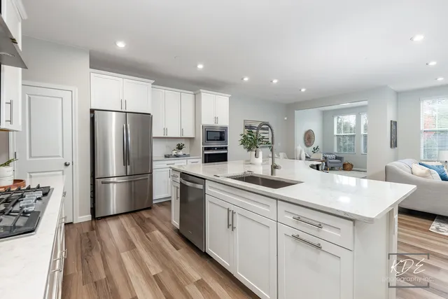 a kitchen with a sink dishwasher a refrigerator and white cabinets with wooden floor