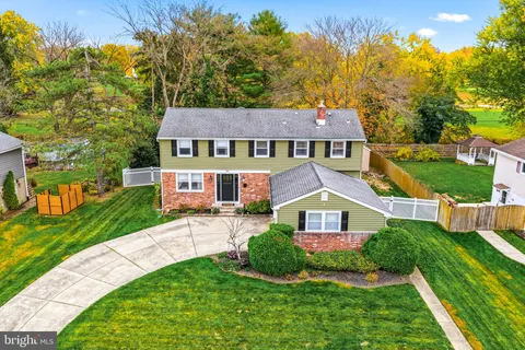 a view of a brick house with a big yard plants and large trees