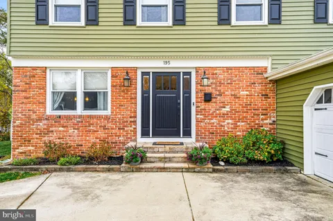 a view of a brick house with small yard plants and large tree