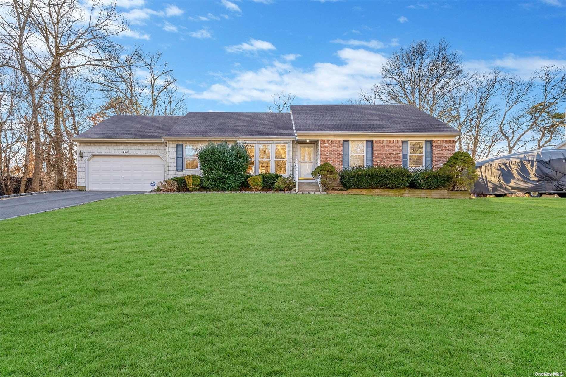 a view of a white house in front of a big yard with plants and large trees