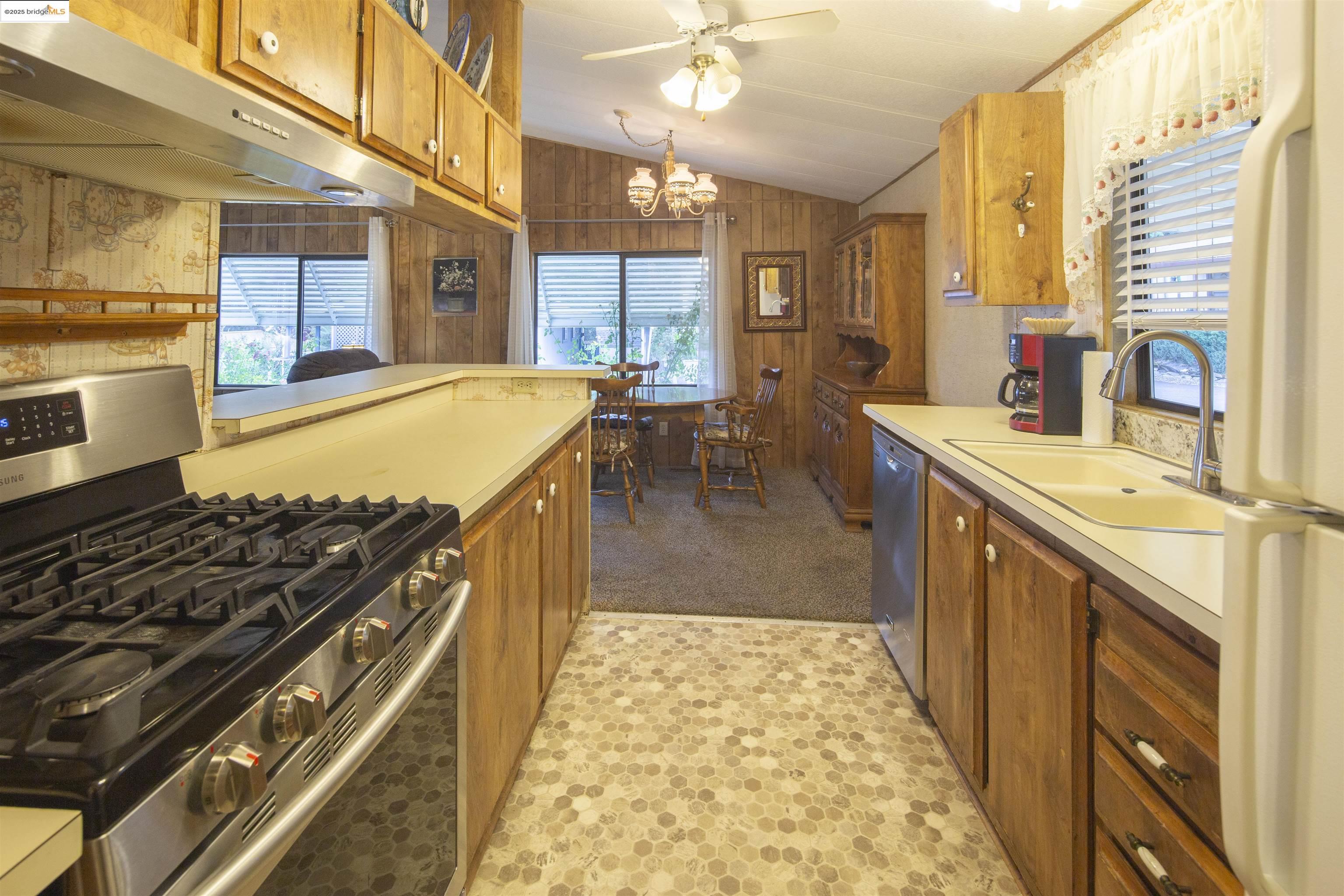 18717 Mill Villa Road, Unit 156 Jamestown, CA 95327 - Photo 13 of 40 Kitchen with stainless steel appliances, under cabinet range hood, wood walls, lofted ceiling, and light countertops