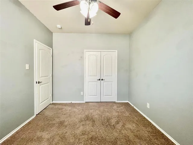an empty room with a ceiling fan and carpet