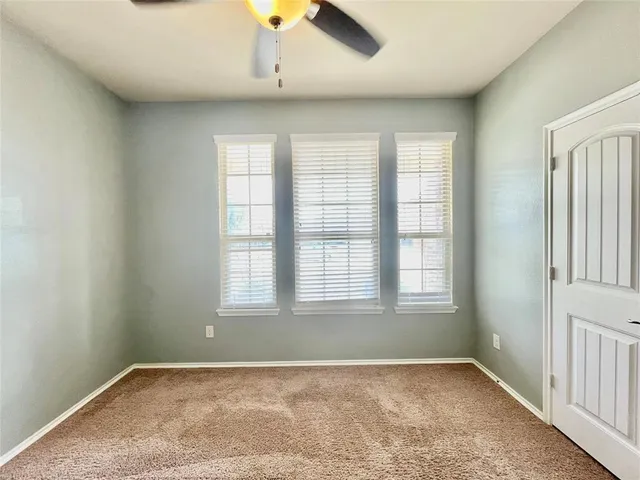 an empty room with chandelier fan and windows