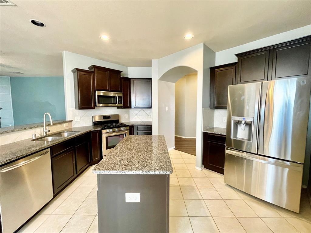 1005 Lake Woodland Drive Little Elm, TX 75068 - Photo 3 of 37 Kitchen with stainless steel appliances, light stone countertops, decorative backsplash, arched walkways, and recessed lighting