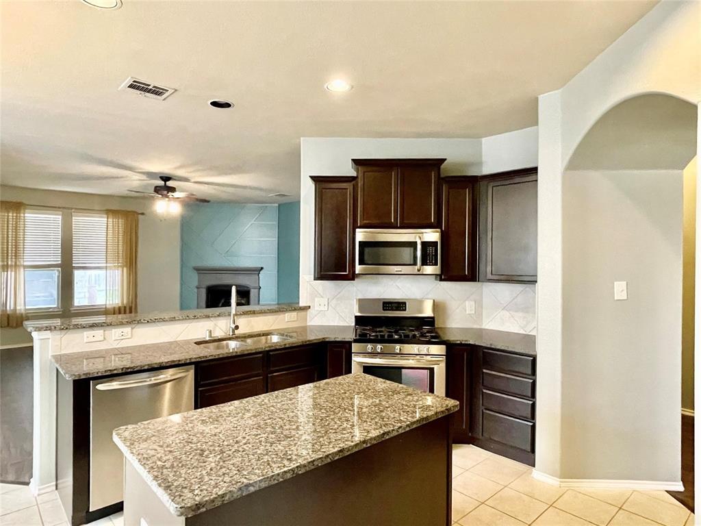 1005 Lake Woodland Drive Little Elm, TX 75068 - Photo 5 of 37 Kitchen featuring light tile patterned floors, tasteful backsplash, a peninsula, light stone counters, and appliances with stainless steel finishes