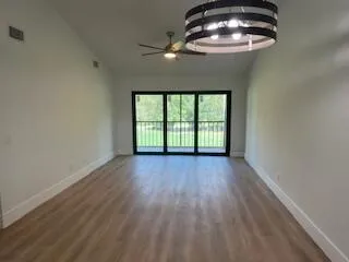 an empty room with a chandelier fan and wooden floor