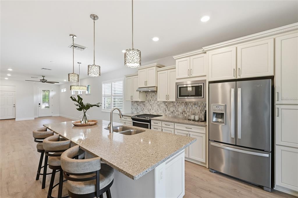 17029 Hampton Falls Terrace Lakewood Ranch, FL 34202 - Photo 20 of 56 a kitchen with stainless steel appliances granite countertop a stove refrigerator a dining table and chairs with wooden floor