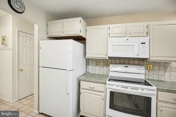 a white refrigerator freezer and a stove sitting inside of a kitchen with granite countertop white cabinets and refrigerator