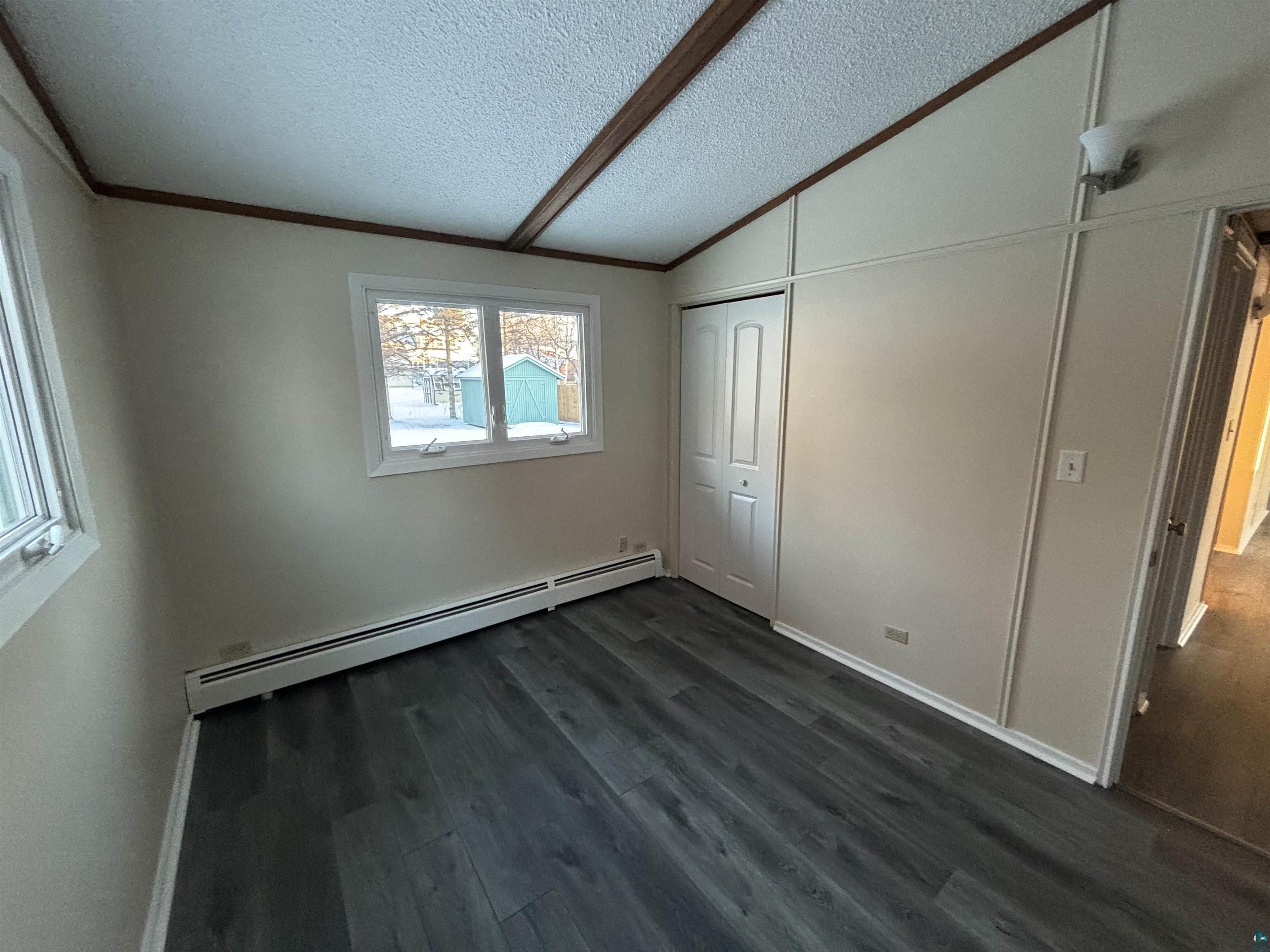 4919 Oakley Street Duluth, MN 55804 - Photo 12 of 20 Unfurnished bedroom with a baseboard heating unit, dark wood finished floors, a textured ceiling, a closet, and vaulted ceiling