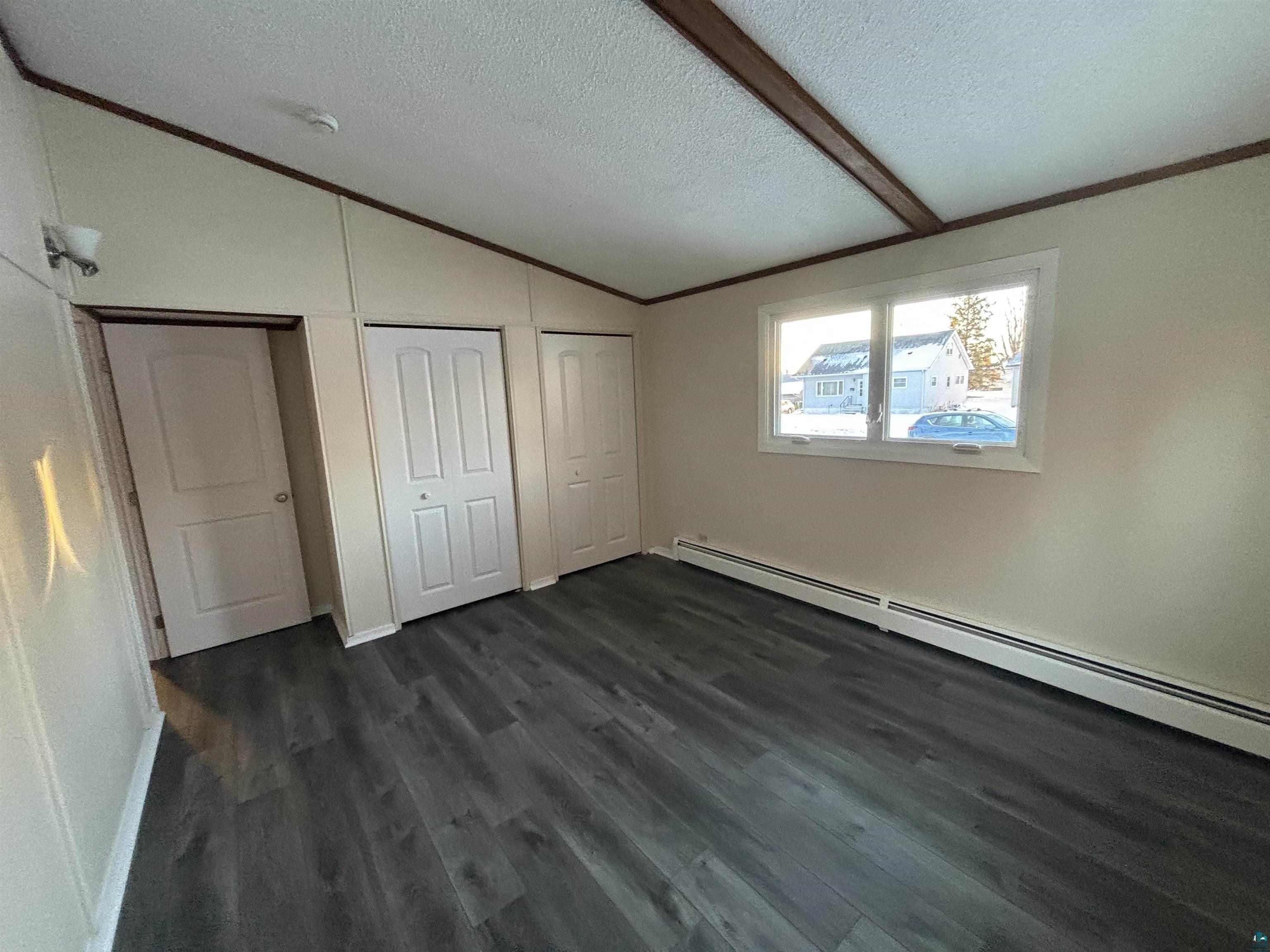 4919 Oakley Street Duluth, MN 55804 - Photo 14 of 20 Unfurnished bedroom with vaulted ceiling, a baseboard radiator, two closets, dark wood-style floors, and a textured ceiling