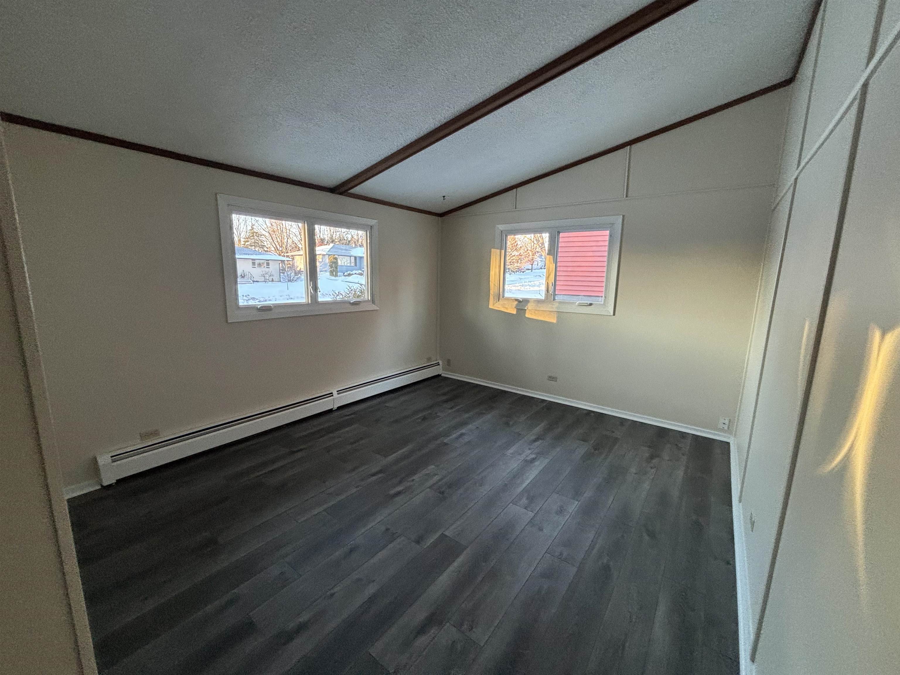 4919 Oakley Street Duluth, MN 55804 - Photo 15 of 20 Empty room featuring a textured ceiling, dark wood finished floors, a baseboard radiator, and lofted ceiling