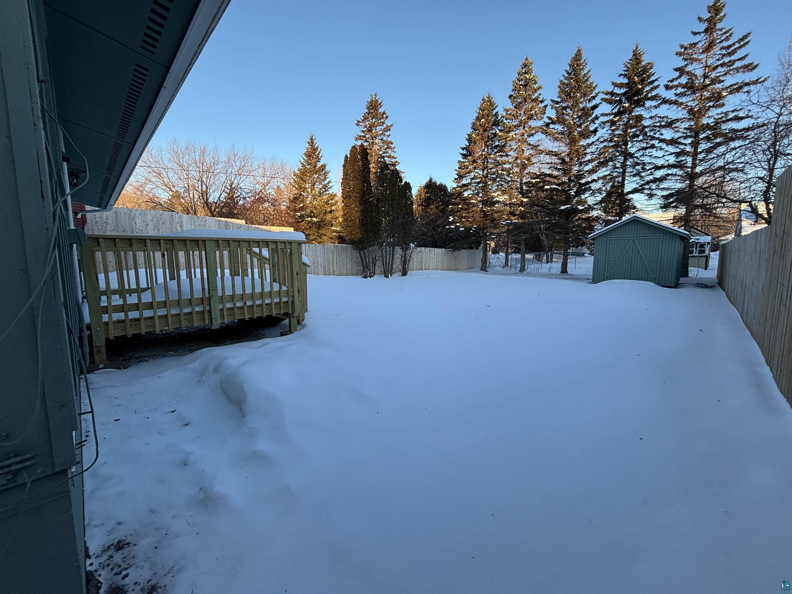 4919 Oakley Street Duluth, MN 55804 - Photo 3 of 20 Yard covered in snow featuring a wooden deck, a fenced backyard, and a shed