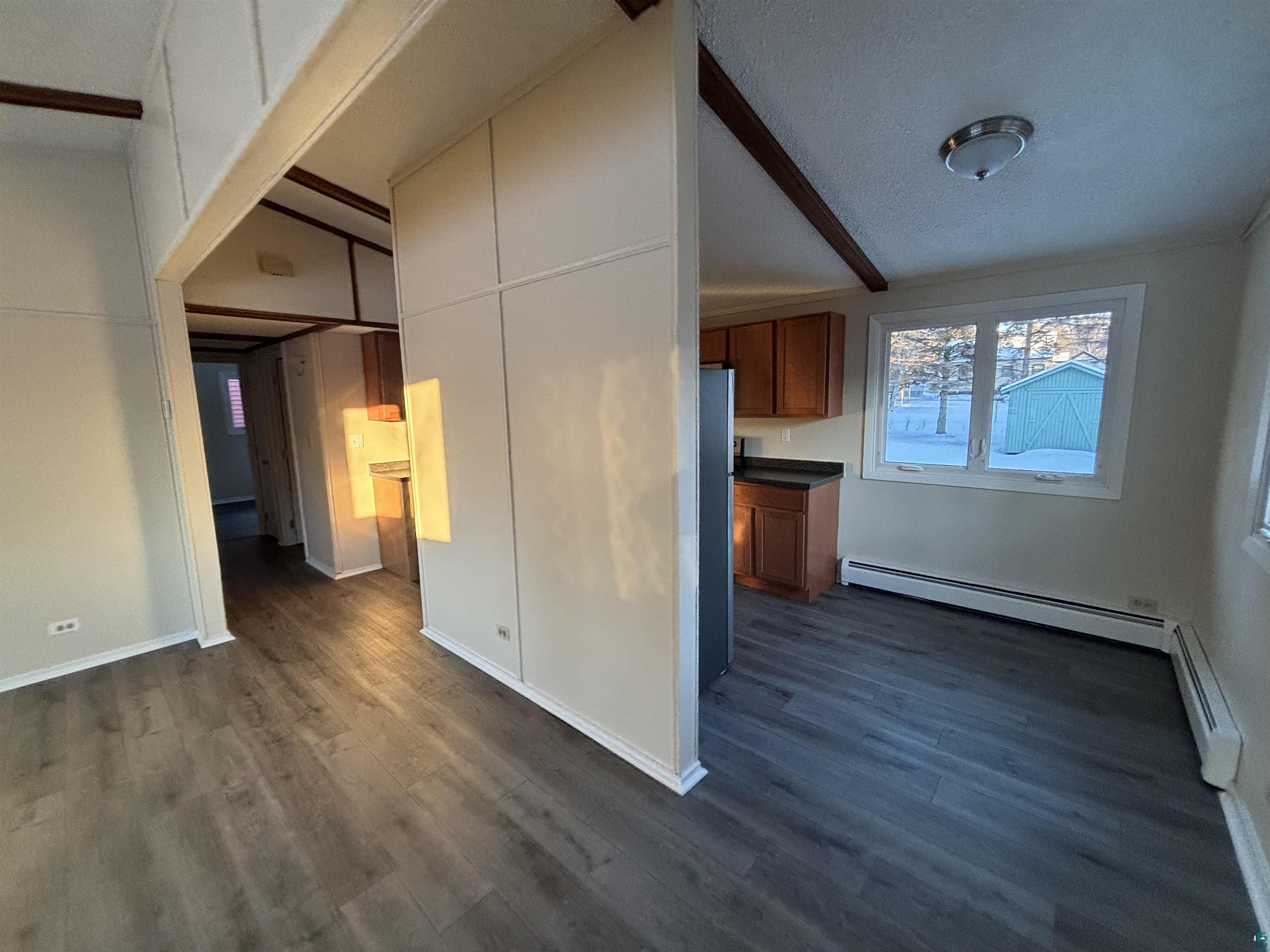 4919 Oakley Street Duluth, MN 55804 - Photo 6 of 20 Kitchen featuring brown cabinetry, dark wood finished floors, freestanding refrigerator, beam ceiling, and a baseboard radiator