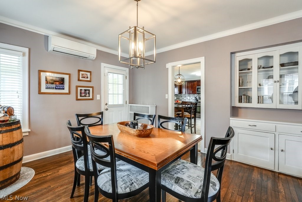 Dining area featuring an inviting chandelier, dark hardwood / wood-style flooring, a wall mounted AC, and ornamental molding