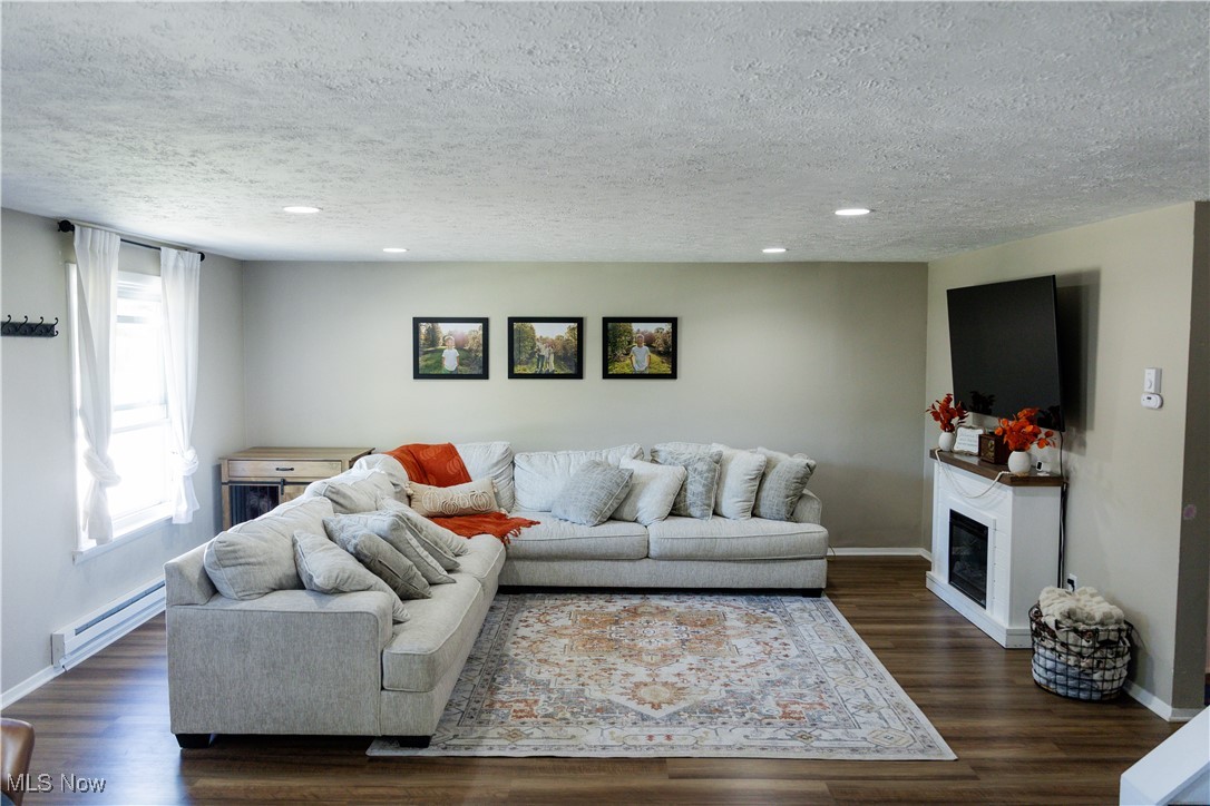 5861 Lee Avenue North Ridgeville, OH 44039 - Photo 5 of 20 Living area featuring a baseboard radiator, dark wood finished floors, a textured ceiling, a glass covered fireplace, and recessed lighting