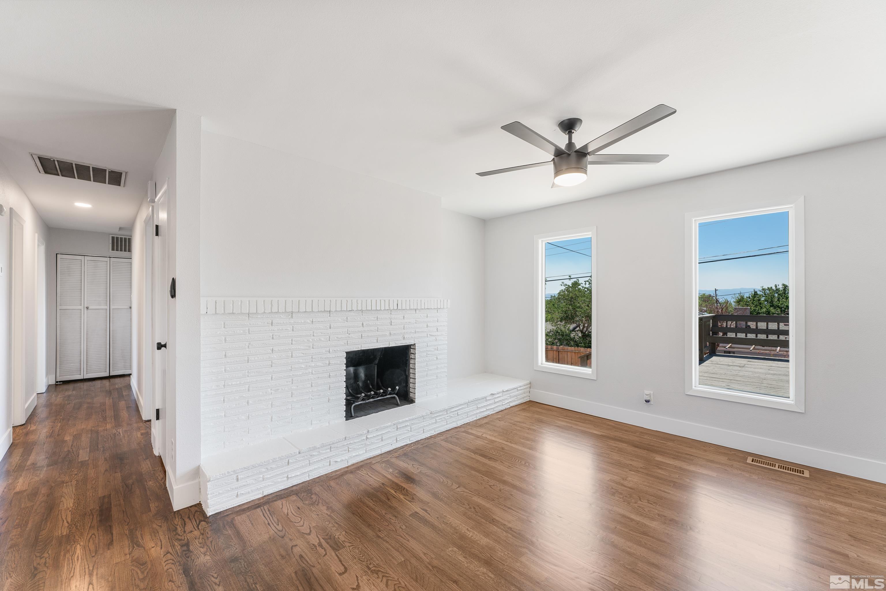 3380 Bryan Street Reno, NV 89503 - Photo 7 of 40 an empty room with wooden floor a ceiling fan with a fireplace and windows