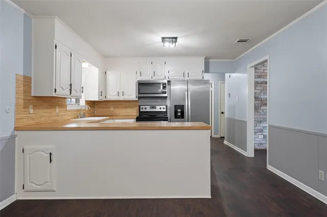 a kitchen with stainless steel appliances granite countertop a refrigerator a stove a sink and white cabinets with wooden floor