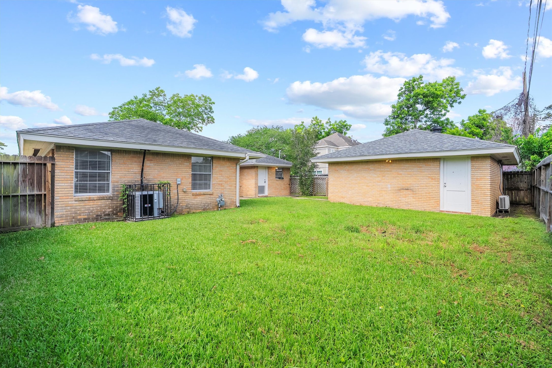 3331 Arbor Street Houston, TX 77004 - Photo 29 of 30 This photo showcases a spacious backyard with lush green grass, bordered by a wooden fence. The exterior of the home features light brick walls and a sloped roof, with a separate structure that could serve as a storage shed or workshop.