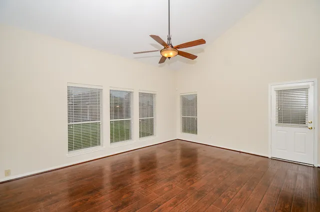 an empty room with wooden floor fan and windows