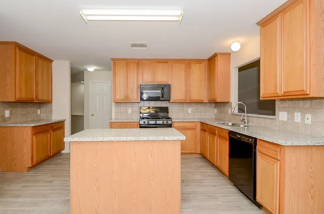 a kitchen with stainless steel appliances granite countertop a stove top oven a sink dishwasher and a refrigerator with wooden floor