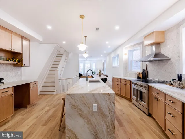 a large kitchen with stainless steel appliances kitchen island a large counter top a stove a chimney a sink and a living room view