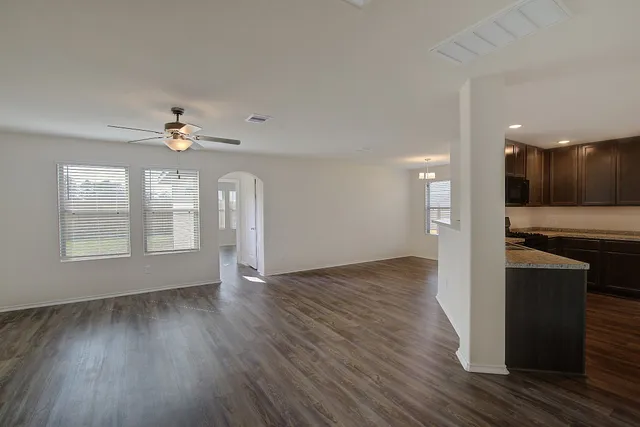 a view of an empty room with wooden floor and a kitchen