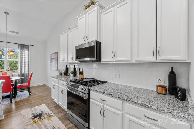 a kitchen with stainless steel appliances granite countertop white cabinets granite counter tops and a wooden floors