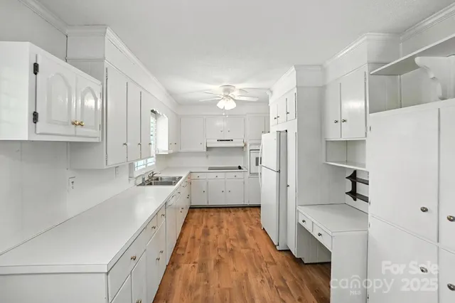 a large white kitchen with a refrigerator a sink dishwasher and white cabinets with wooden floor