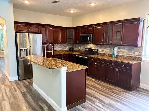 a kitchen with stainless steel appliances granite countertop a stove a refrigerator and a sink with wooden cabinets