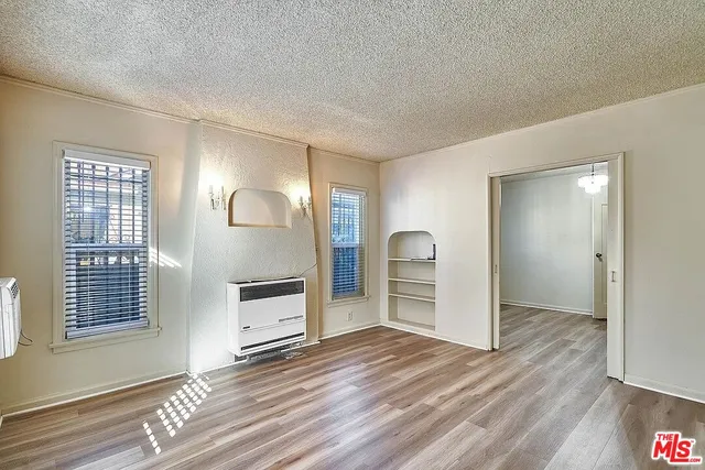 an empty room with wooden floor cabinet and windows