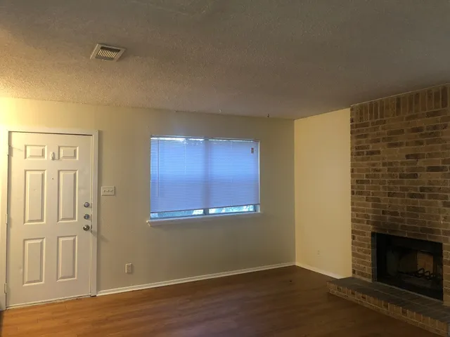 a view of an empty room with wooden floor and a fireplace
