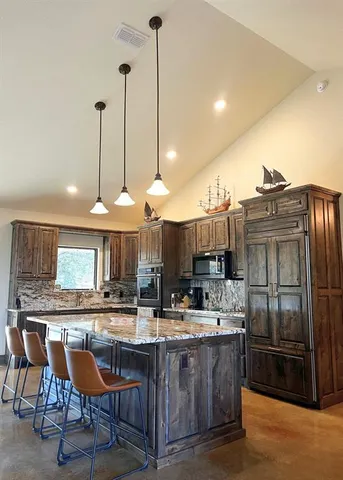 a kitchen with stainless steel appliances granite countertop a sink a stove a refrigerator and chairs