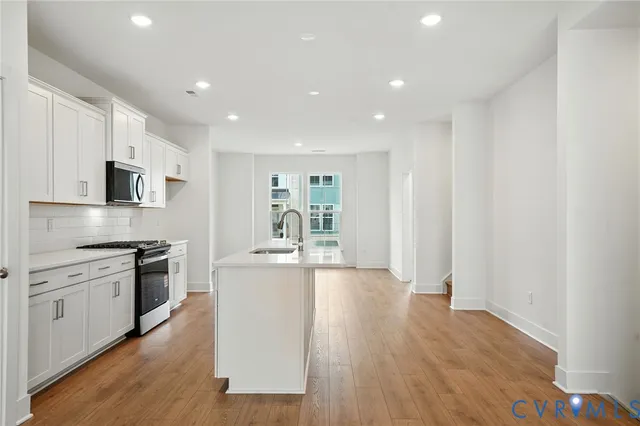 a kitchen with stainless steel appliances granite countertop a stove top oven a sink dishwasher and a refrigerator with wooden floor