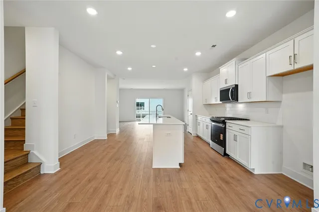 a kitchen with stainless steel appliances granite countertop a stove top oven a sink dishwasher and a refrigerator with wooden floor