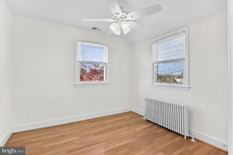 an empty room with wooden floor chandelier fan and windows