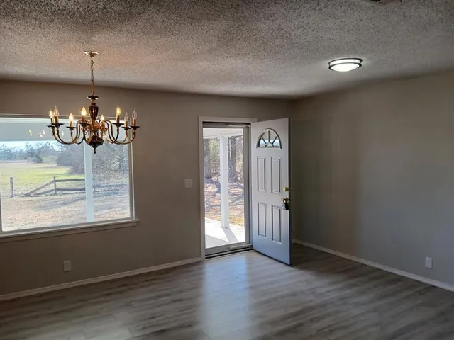 an empty room with wooden floor chandelier and windows