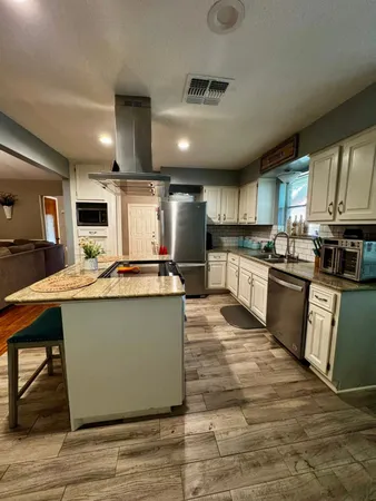 a kitchen with kitchen island granite countertop a stove top oven a sink dishwasher a dining table and chairs with wooden floor