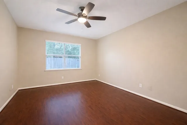 an empty room with wooden floor fan and windows