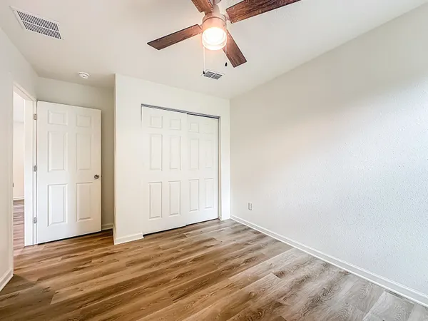 an empty room with wooden floor ceiling fan and windows