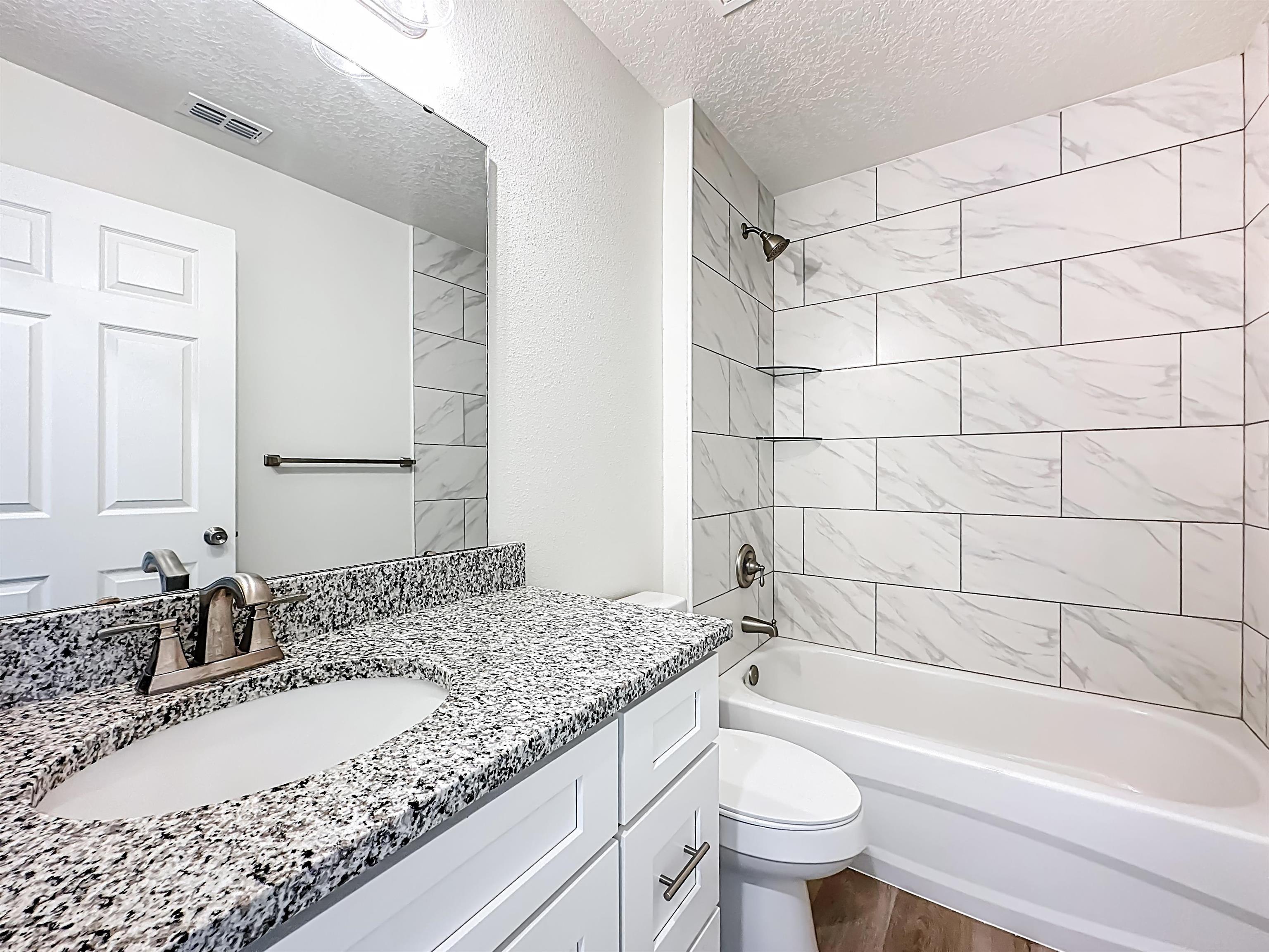 780 West 5th Street St. Augustine, FL 32084 - Photo 17 of 30 a bathroom with a granite countertop sink a toilet a mirror a bathtub and shower
