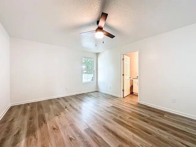 an empty room with wooden floor ceiling fan and windows