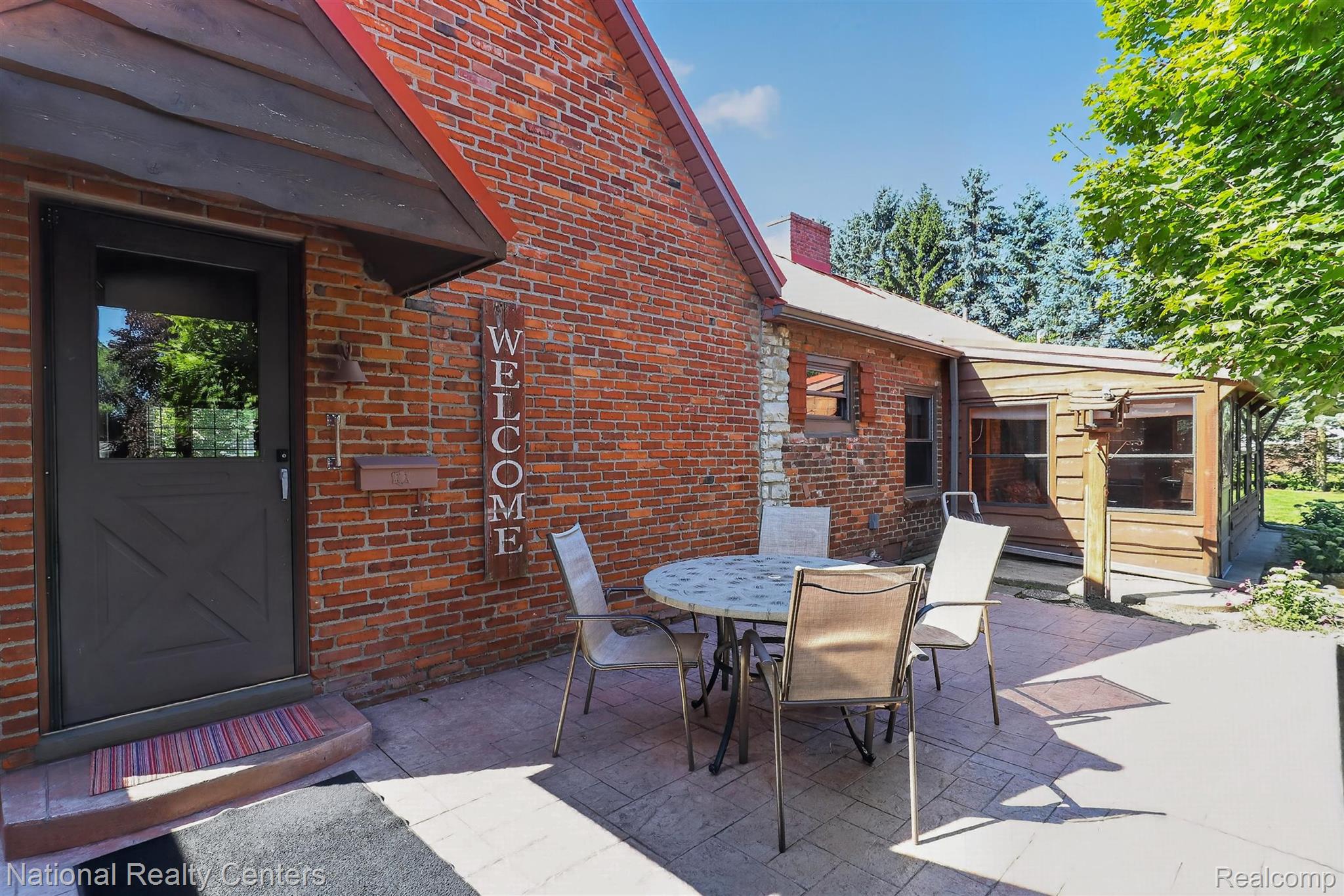 127 West Albain Road Petersburg, MI 49270 - Photo 53 of 61 Brick exterior with a red roof, a dark entry door with a window, and a stamped concrete patio